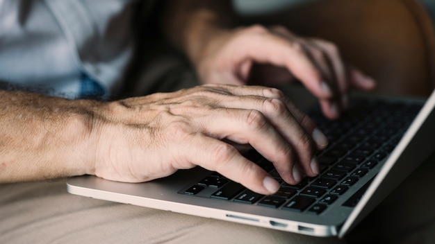 Die Hand eines älteren Mannes, die auf Laptop schreibt