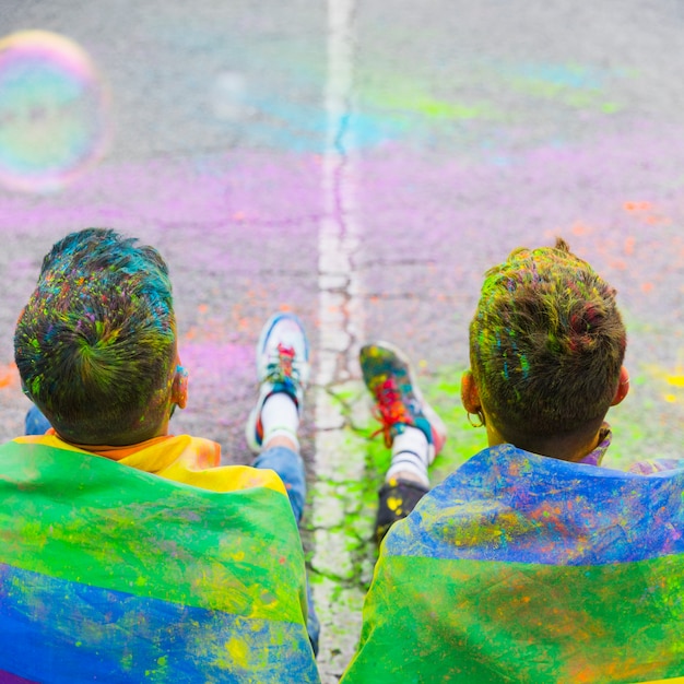 Kostenloses Foto die homosexuellen paare, die auf straße sitzen, bedeckten regenbogenflagge