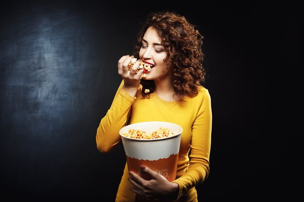 Die hungrige Frau isst eine Handvoll Popcorn, während sie auf den Film wartet