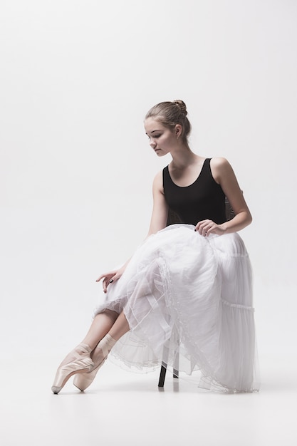 Die jugendlich Ballerina in der weißen Packung sitzt auf Stuhl