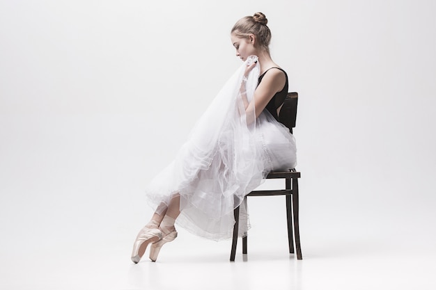Die jugendlich Ballerina in der weißen Packung sitzt auf Stuhl