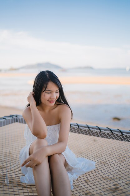 Die junge asiatische Frau, die auf Hängematte sitzt, entspannen sich auf Strand, schönes weibliches glückliches sich entspannen nahe Meer.