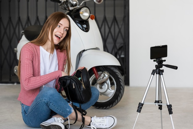 Die junge Bloggerin zeichnet sich auf, wie sie mit ihrer Tasche neben ihrem Motorrad sitzt