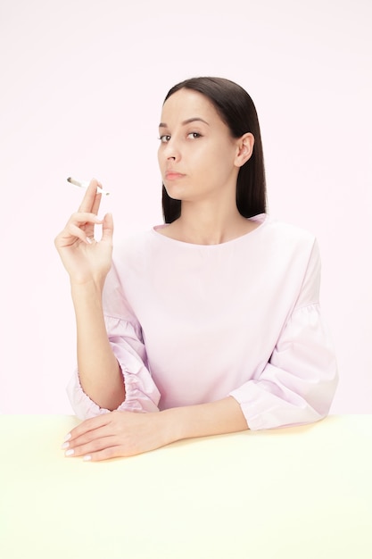 Die junge Frau, die Zigarette raucht, während sie am Tisch im Studio sitzt.