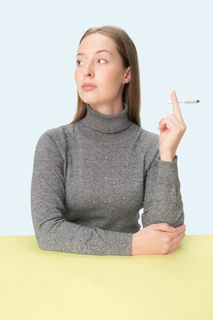 Die junge Frau, die Zigarette raucht, während sie am Tisch im Studio sitzt.