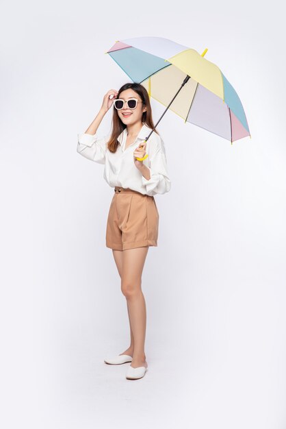 Die junge Frau trug ein weißes Hemd und Shorts, einen Hut und eine Brille und breitete einen Regenschirm aus
