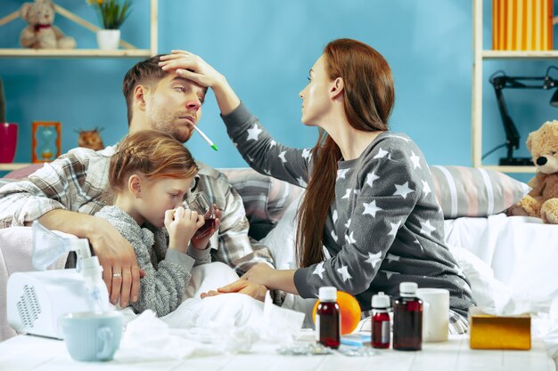 Die junge Frau und der Mann mit der kranken Tochter zu Hause. Behandlung zu Hause. Mit einer Krankheit kämpfen. Medizinische Gesundheitsversorgung. Familienhaftigkeit. Der Winter, Influenza, Gesundheit, Schmerz, Elternschaft, Beziehungskonzept