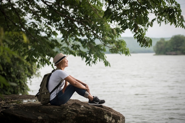 Die junge glückliche Frau, die mit Rucksack sitzt, genießen die Natur nach Wanderung.