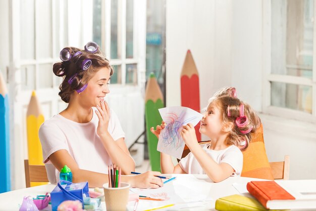 Die junge Mutter und ihre kleine Tochter zeichnen zu Hause mit Bleistiften