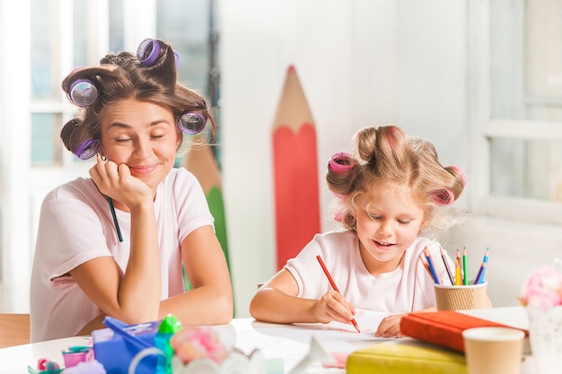 Die junge Mutter und ihre kleine Tochter zeichnen zu Hause mit Bleistiften