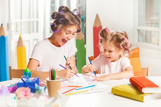 Die junge Mutter und ihre kleine Tochter zeichnen zu Hause mit Bleistiften