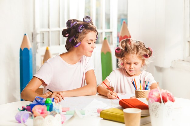 Die junge Mutter und ihre kleine Tochter zeichnen zu Hause mit Bleistiften