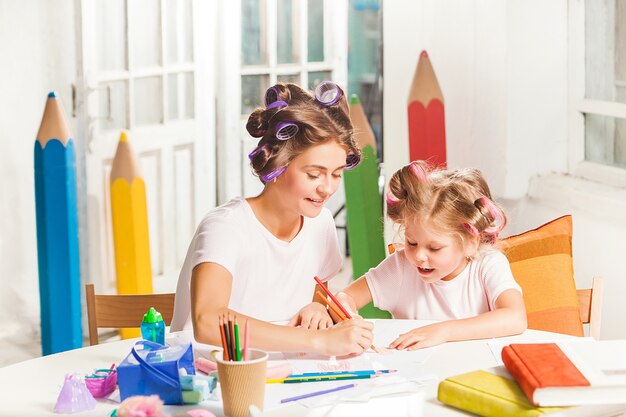 Die junge Mutter und ihre kleine Tochter zeichnen zu Hause mit Bleistiften