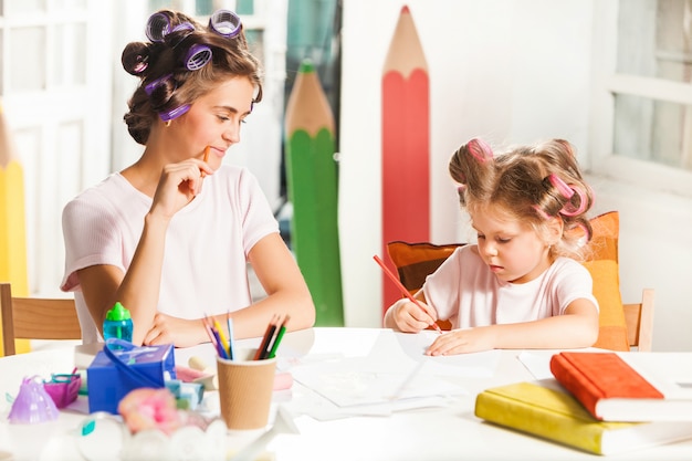 Die junge Mutter und ihre kleine Tochter zeichnen zu Hause mit Bleistiften