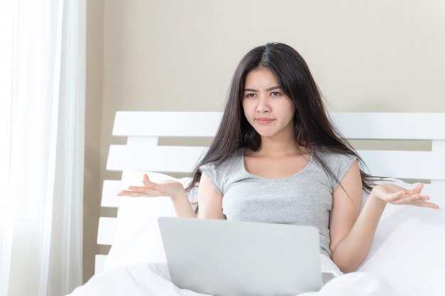 Die junge Schönheit, die auf Bett sitzt, benutzt sie slaptop und fühlt sich ernst und traurig