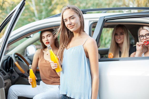 Die jungen Frauen im Auto lächeln und trinken Saft