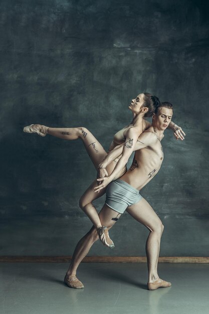 Die jungen modernen Balletttänzer mit Tätowierungen auf Körpern, die auf grauem Studiohintergrund posieren