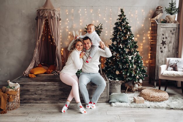 Die kaukasische Familie spielt mit ihrem kleinen Kind in einem Wohnzimmer mit einem Weihnachtsbaum zu Hause