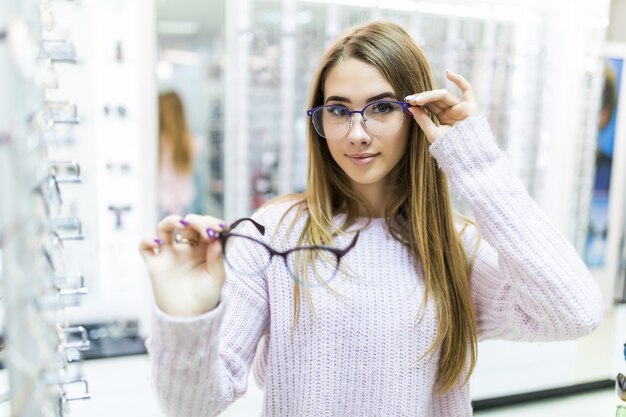 Die kleine Dame in einem weißen Pullover hält eine medizinische Brille im Arm und schaut sie sich in einem speziellen Geschäft an