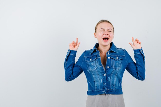 Die lachende junge Frau hebt ihre Zeigefinger auf weißem Hintergrund