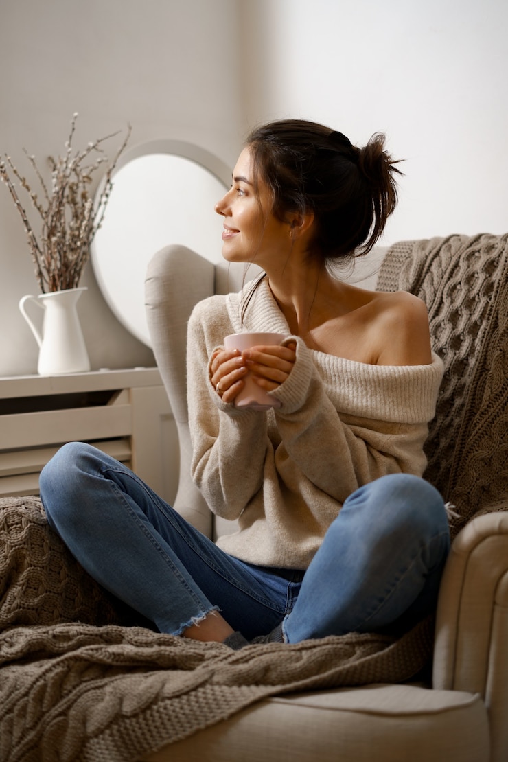 Kostenlose Foto die lächelnde dame in schicker, trendiger kleidung sitzt mit einer tasse tee auf dem sessel.
