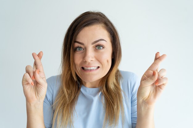 Die lächelnde hübsche Frau, die gekreuzte Finger zeigt, gestikulieren. Dame macht Wunsch.