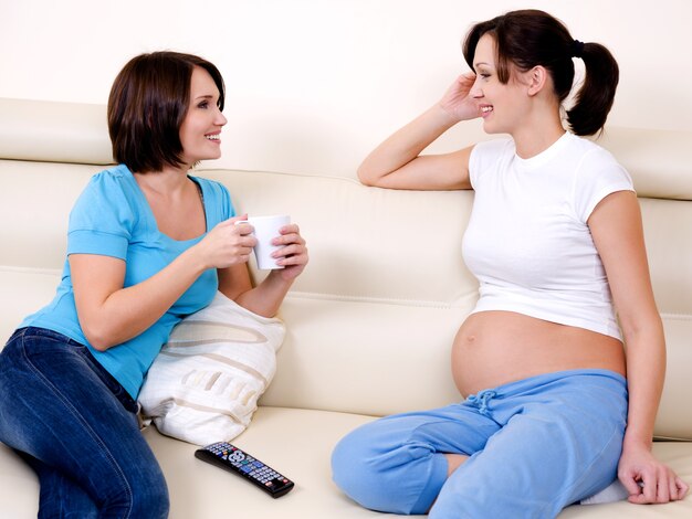 Die lächelnde schwangere Frau kommuniziert mit der Freundin - drinnen