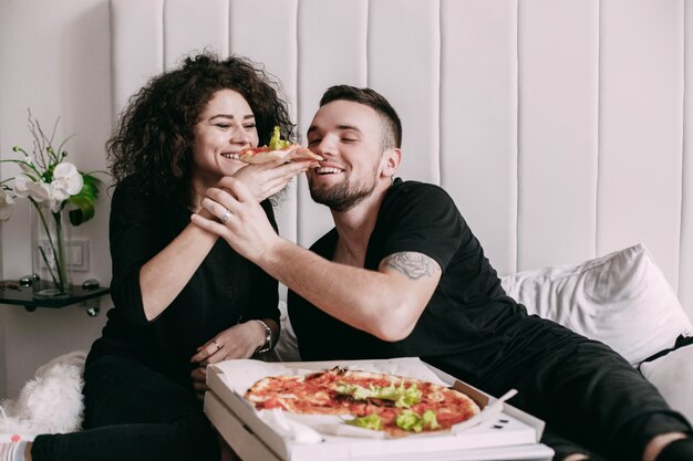 Die lockige Frau gibt ihrem Mann ein Stück Pizza