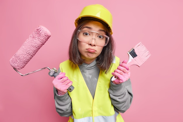 Die Malerin sieht unglücklich aus, schürzt die Lippen und hält Pinsel und Walze in Uniform, um das Haus neu zu dekorieren