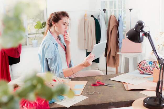 Die Modedesignerin, die im Studio arbeitet, sitzt auf dem Schreibtisch