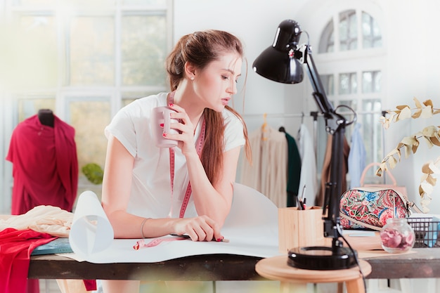 Die Modedesignerin, die im Studio arbeitet, sitzt auf dem Schreibtisch