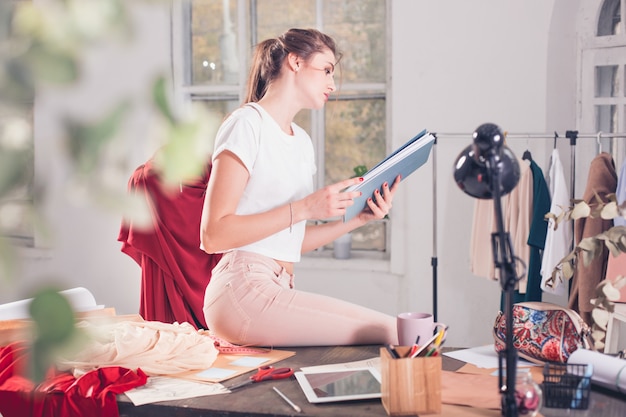 Die Modedesignerin, die im Studio arbeitet, sitzt auf dem Schreibtisch