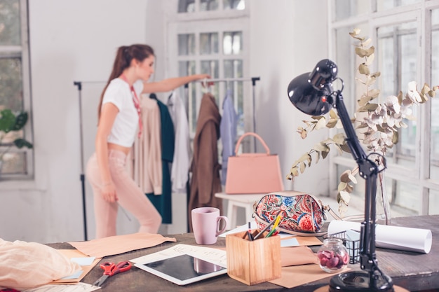 Die Modedesignerin, die im Studio arbeitet, sitzt auf dem Schreibtisch