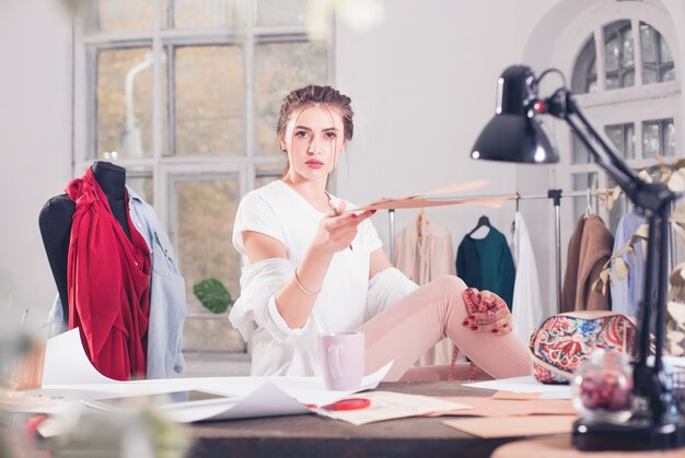 Die Modedesignerin, die im Studio arbeitet, sitzt auf dem Schreibtisch