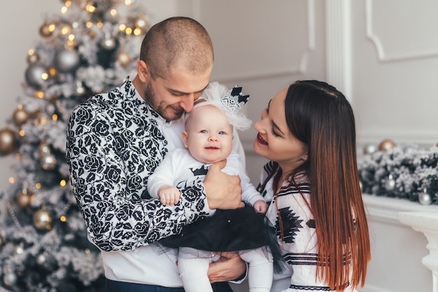 Die Mutter und der Vater, die ihre Tochter umfassen und nahe Weihnachtsbaum stehen