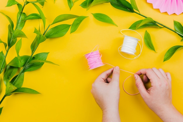 Kostenloses Foto die nahaufnahme der hand der frau rosa threadspule mit grün halten verlässt auf gelbem hintergrund