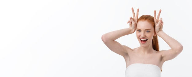 Kostenloses Foto die nahaufnahme einer schönen jungen frau mit einem badetuch, das ihre brüste auf grau bedeckt, zeigt zwei fingerzeichen