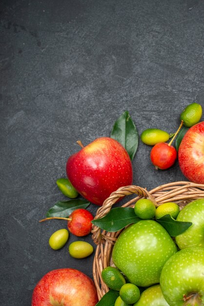 Die Nahaufnahme zeigt den Korb mit grünen Äpfeln neben den Zitrusfrüchten mit roten Äpfeln, Kirschen und Früchten