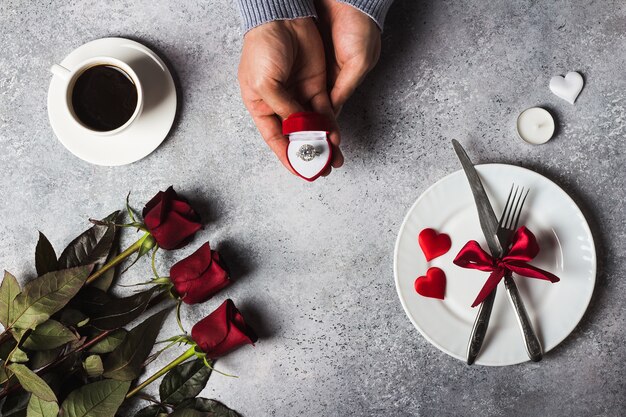 Die romantische Abendessengedeck-Mannhand des Valentinstags, die Verlobungsring im Kasten hält, heiraten mich