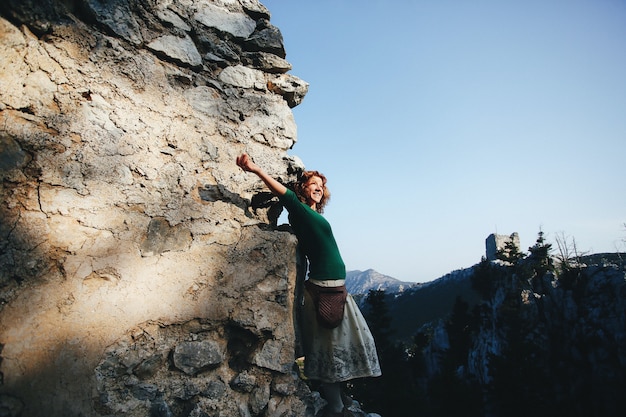 Die rothaarige Frau beugt sich zum Felsen und schaut in die Sonne