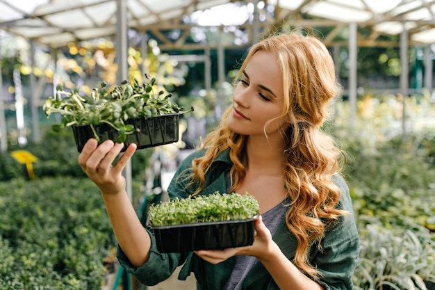 Die rothaarige süße Dame untersucht intensiv immergrüne kleine Pflanzen. Nahaufnahmeporträt des Modells der europäischen Erscheinung im Garten.