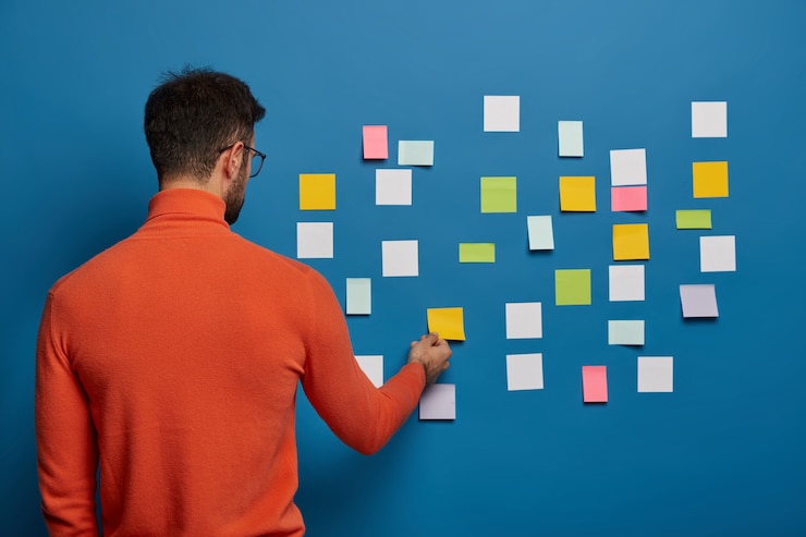 Kostenlose Foto die rückansicht männlicher professioneller arbeiten bringt seine ideen auf haftnotizen und schreibt hauptinformationen für die erstellung eines geschäftsplans
