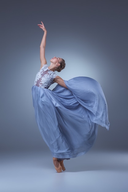 Die schöne Ballerina, die im langen blauen Kleid auf blauem Hintergrund tanzt