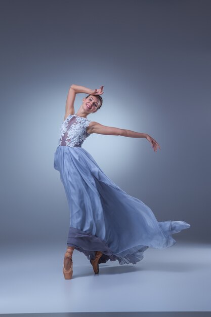 Die schöne Ballerina, die im langen blauen Kleid auf blauem Hintergrund tanzt