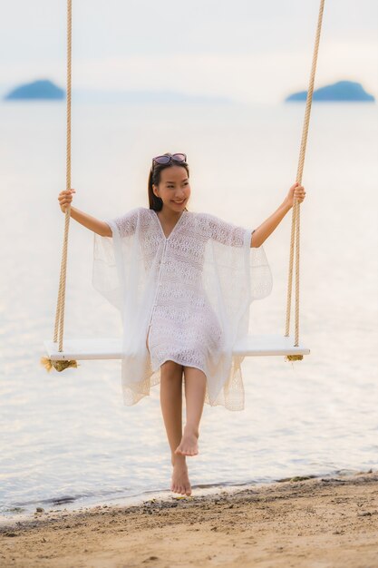 Die schöne junge asiatische Frau des Porträts, die auf dem Schwingen um Strandseeozean für sitzt, entspannen sich