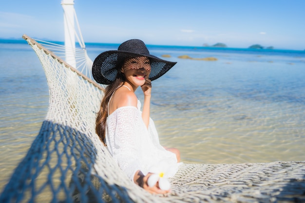 Kostenloses Foto die schöne junge asiatische frau des porträts, die auf hängematte um seestrandozean für sitzt, entspannen sich