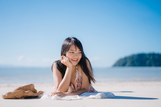 Die schöne junge asiatische Frau, die auf dem glücklichen Strand liegt, entspannen sich nahe Meer.