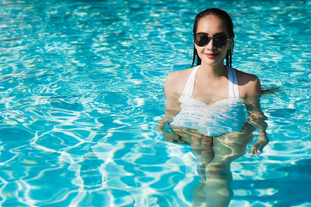 Die schöne junge asiatische Frau, die glücklich ist und Lächeln im Swimmingpool für entspannen sich Reise und Ferien