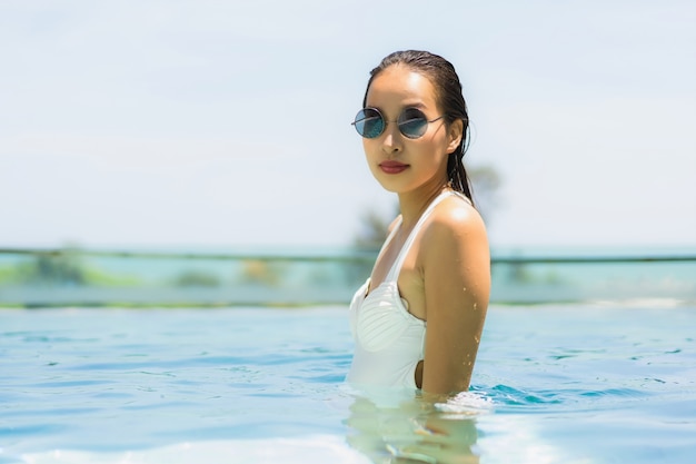 Die schöne junge asiatische Frau, die glücklich ist und Lächeln im Swimmingpool für entspannen sich Reise und Ferien