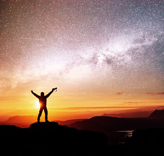 Die Silhouette der Frau steht oben auf dem Berg und zeigt auf die Milchstraße vor Sonnenaufgang und genießt mit buntem Nachthimmel